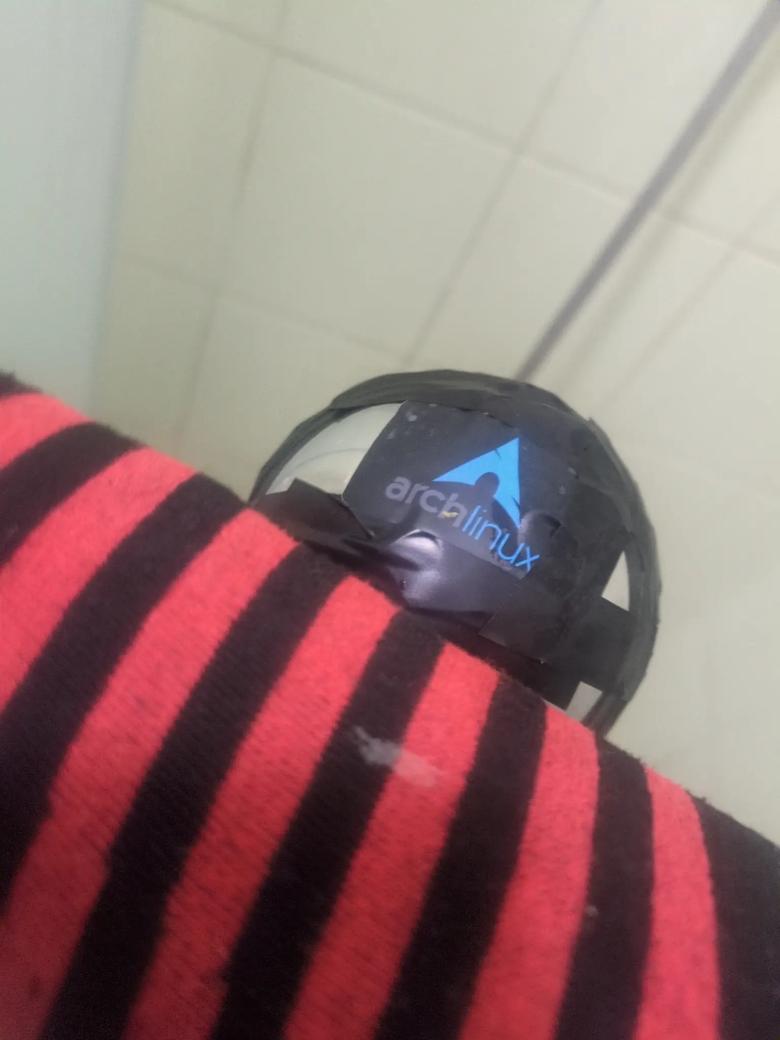 Shower head back, half covered by red black stripped sleeve. Arch Linux sticker on it and plenty of tape.